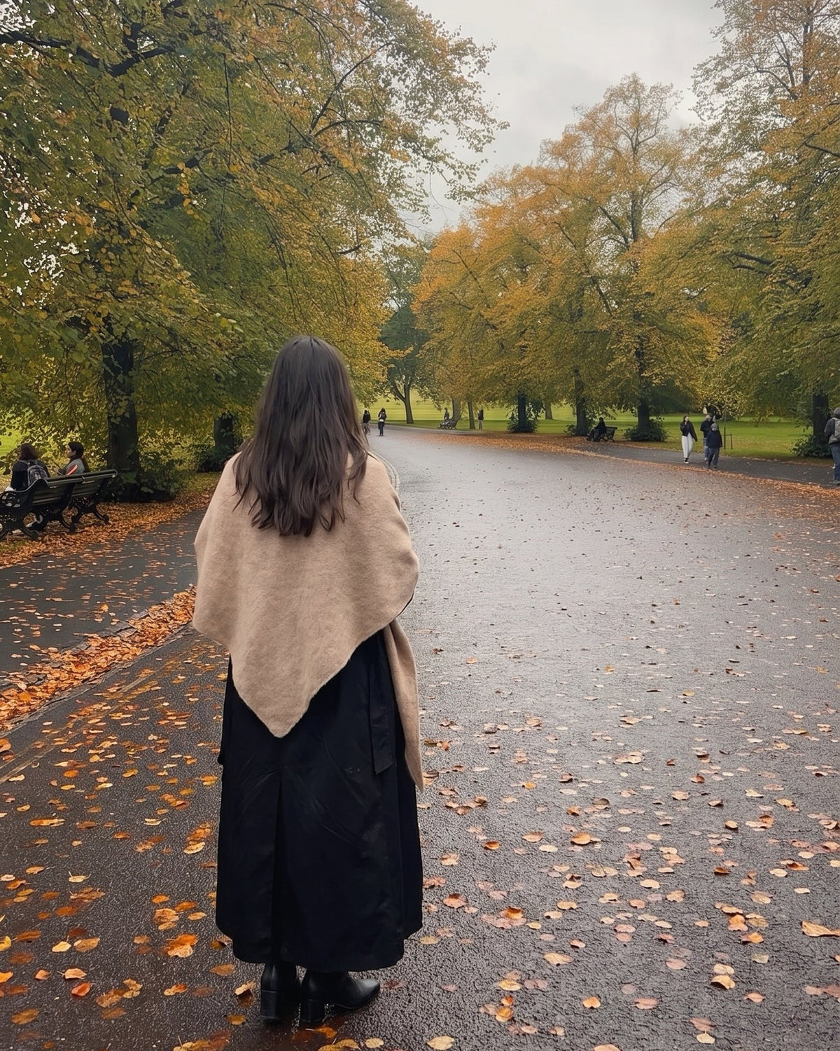 A woman in a khaki Fleece Shawl over her coat, seen from behind on an autumn path