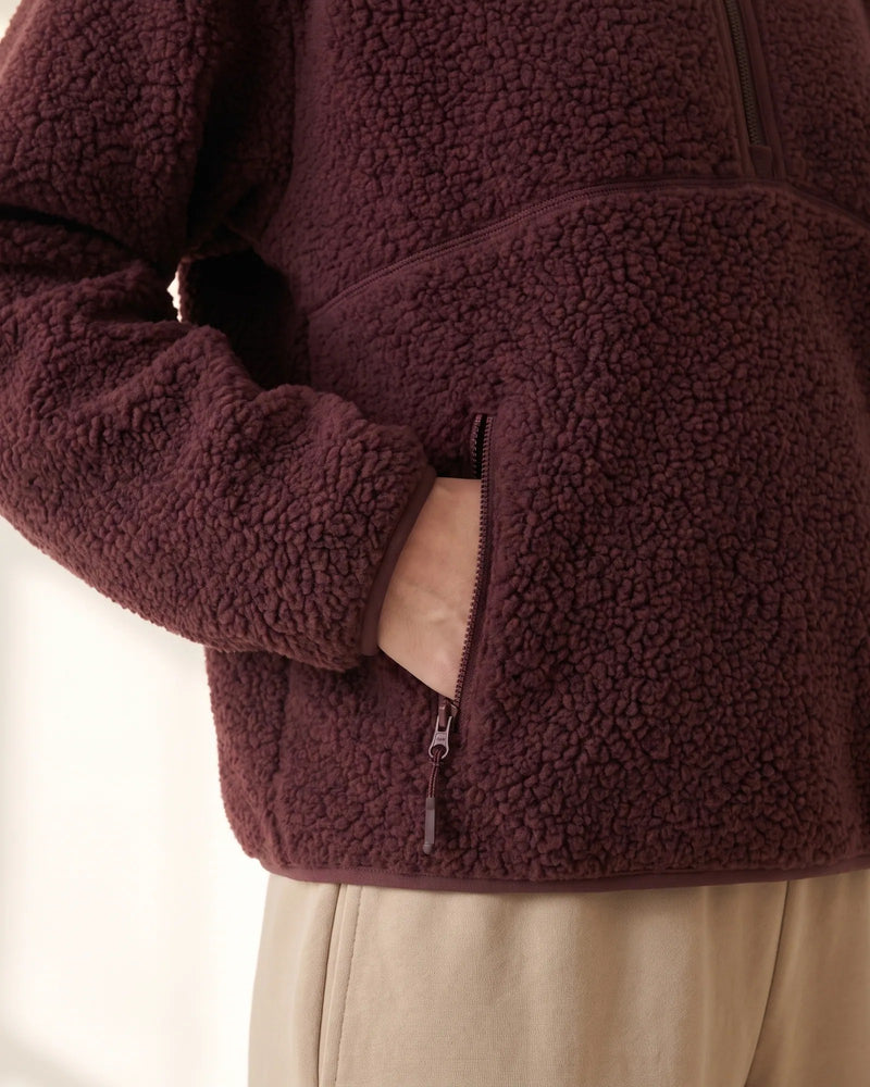 Hand in the zip pocket of the burgundy sherpa half-zip, with the bound hem below