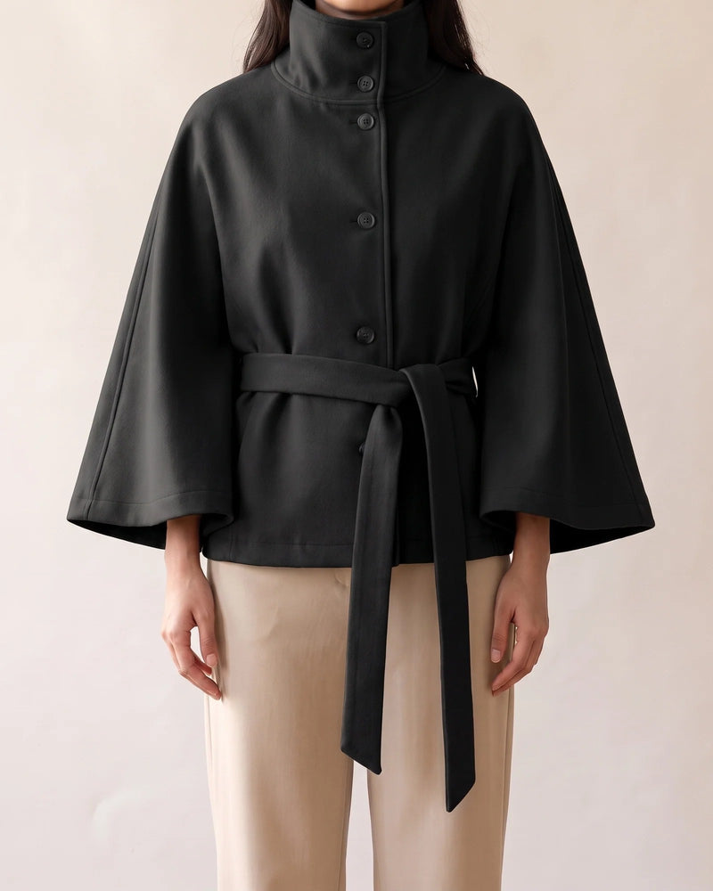 The black cape coat from the front, showing the wide cape sleeves, the tie belt and the curved hem