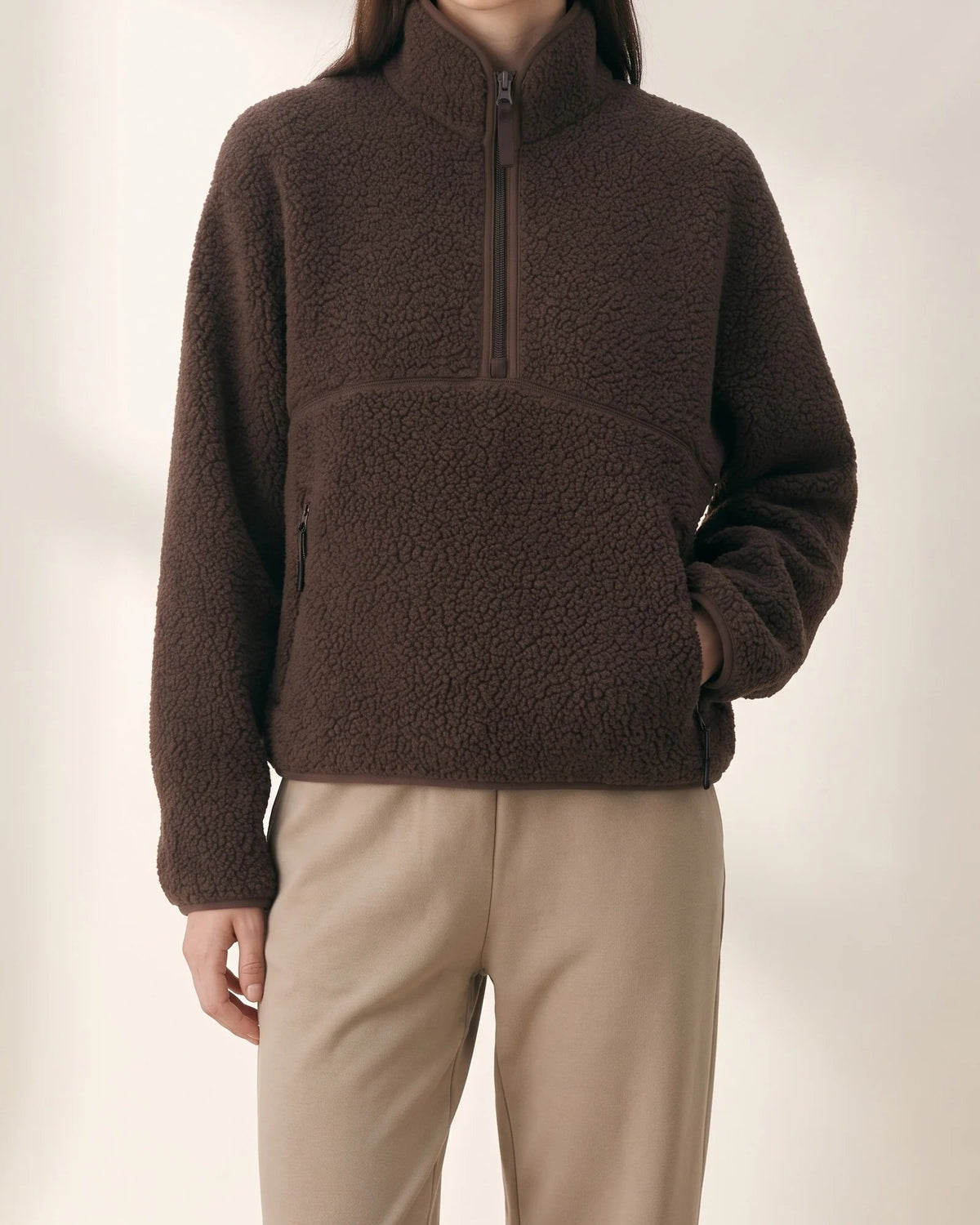 Chocolate cropped sherpa half-zip with a tall funnel collar, hand in the zip pocket