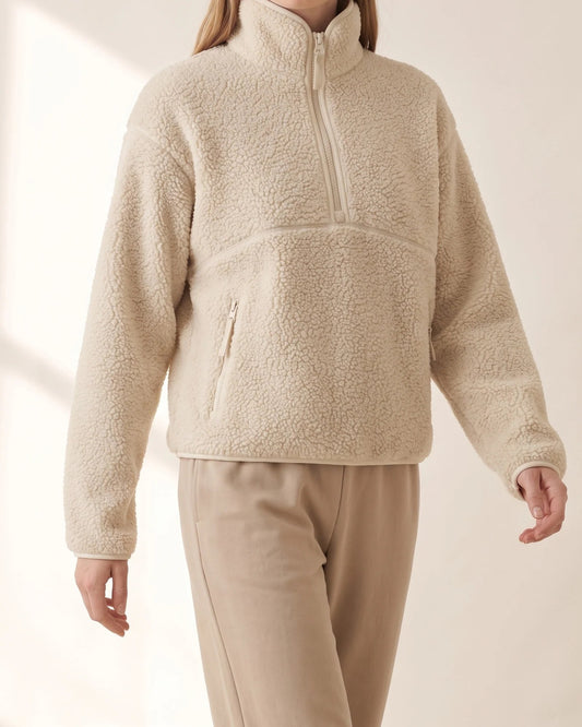 Cream sherpa half-zip pullover worn mid-stride with stone trousers