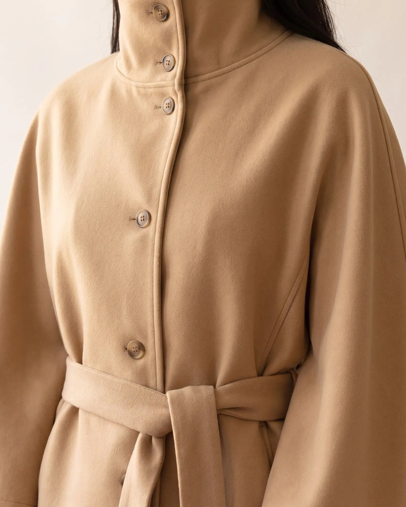 Close view of the camel cape coat showing the tall funnel collar with two buttons and the button front
