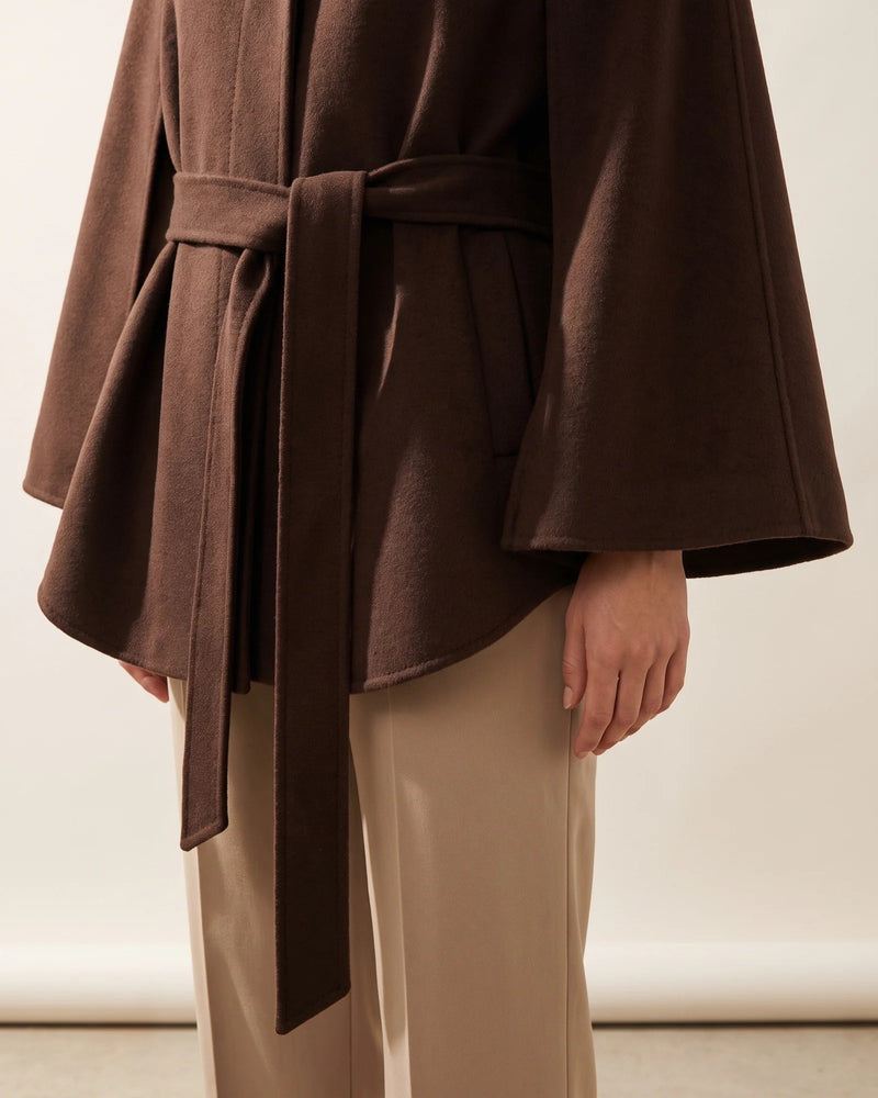 The tie belt knotted at the waist of the chocolate cape coat, with a cape sleeve falling beside it