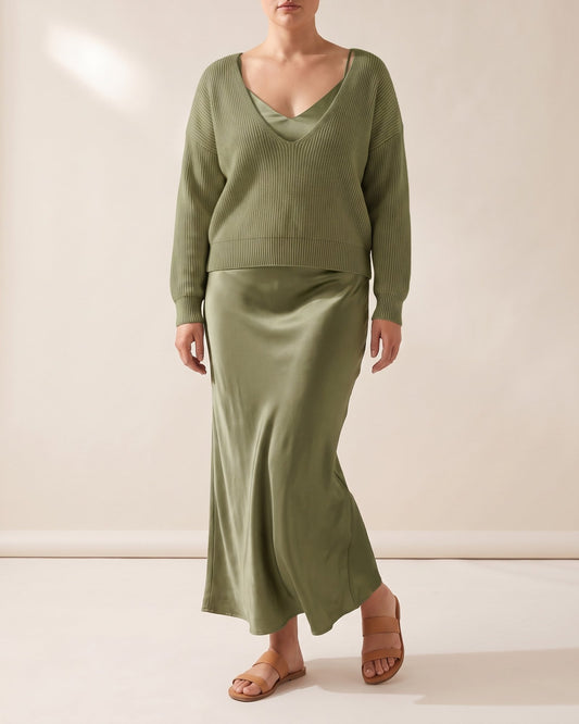 Woman in the olive Sloane set in the studio: V-neck rib knit sweater over an ankle-length satin slip dress
